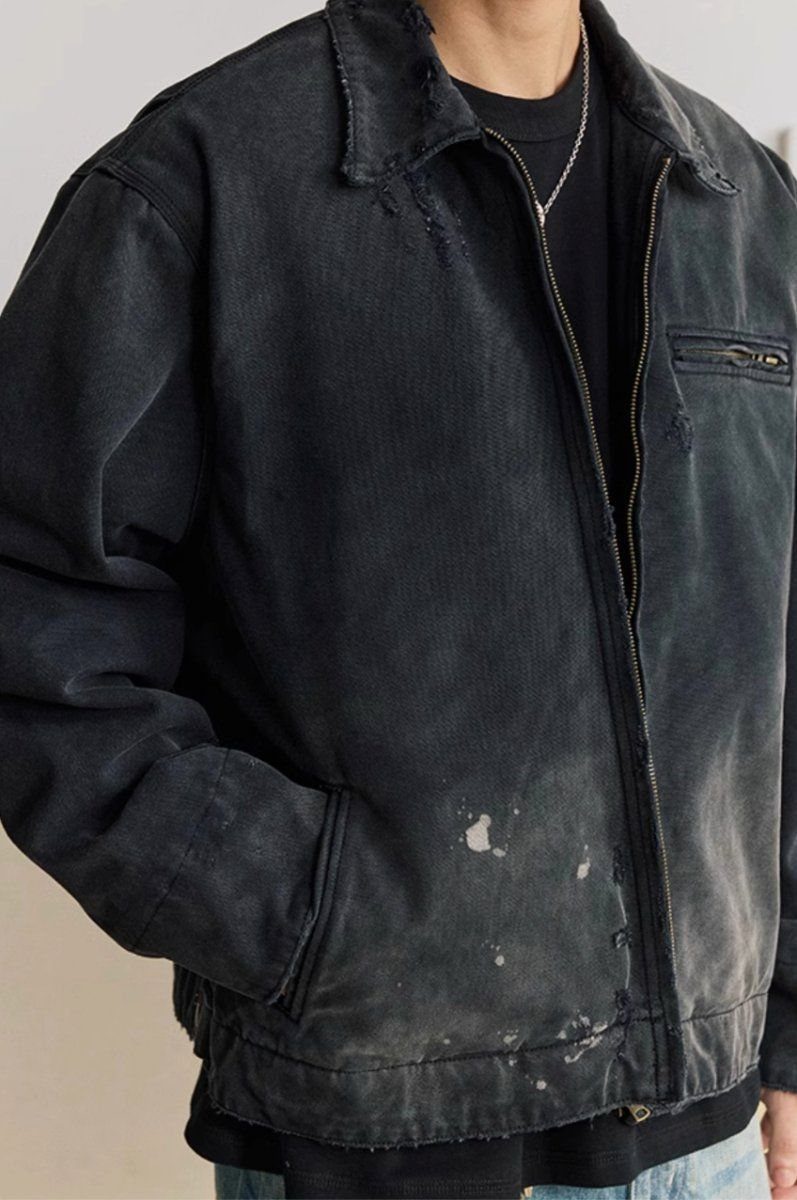 A person wearing a black distressed denim jacket with visible white paint splatters and frayed collar edges.