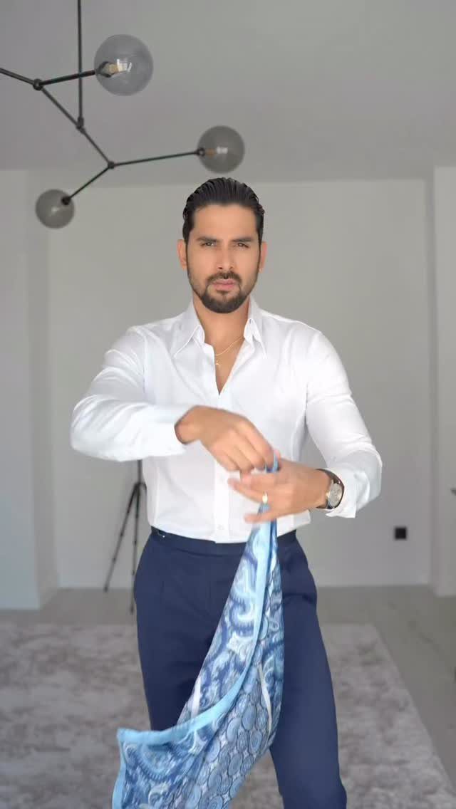 A man holding a large blue patterned silk fabric to style as a cravat or ascot.