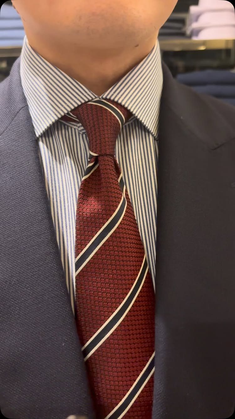 A man wearing a navy suit, striped shirt, and a burgundy striped necktie.