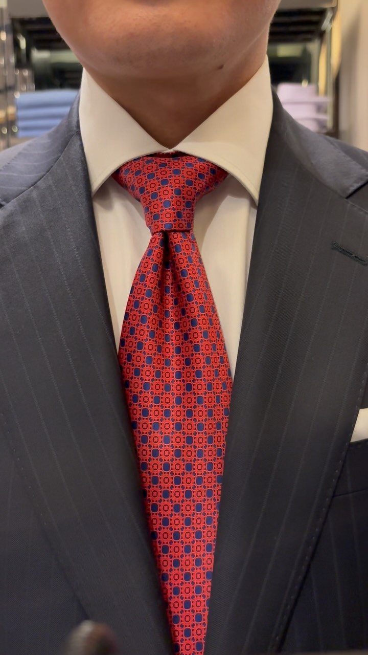 A man wearing a red patterned silk necktie with a large, symmetrical knot and a pinstripe suit.