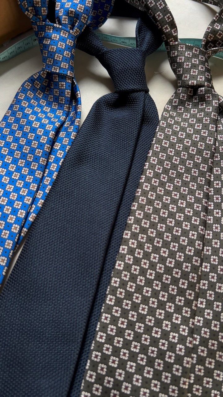 Three patterned and solid neckties in blue, navy, and olive green laid side by side.