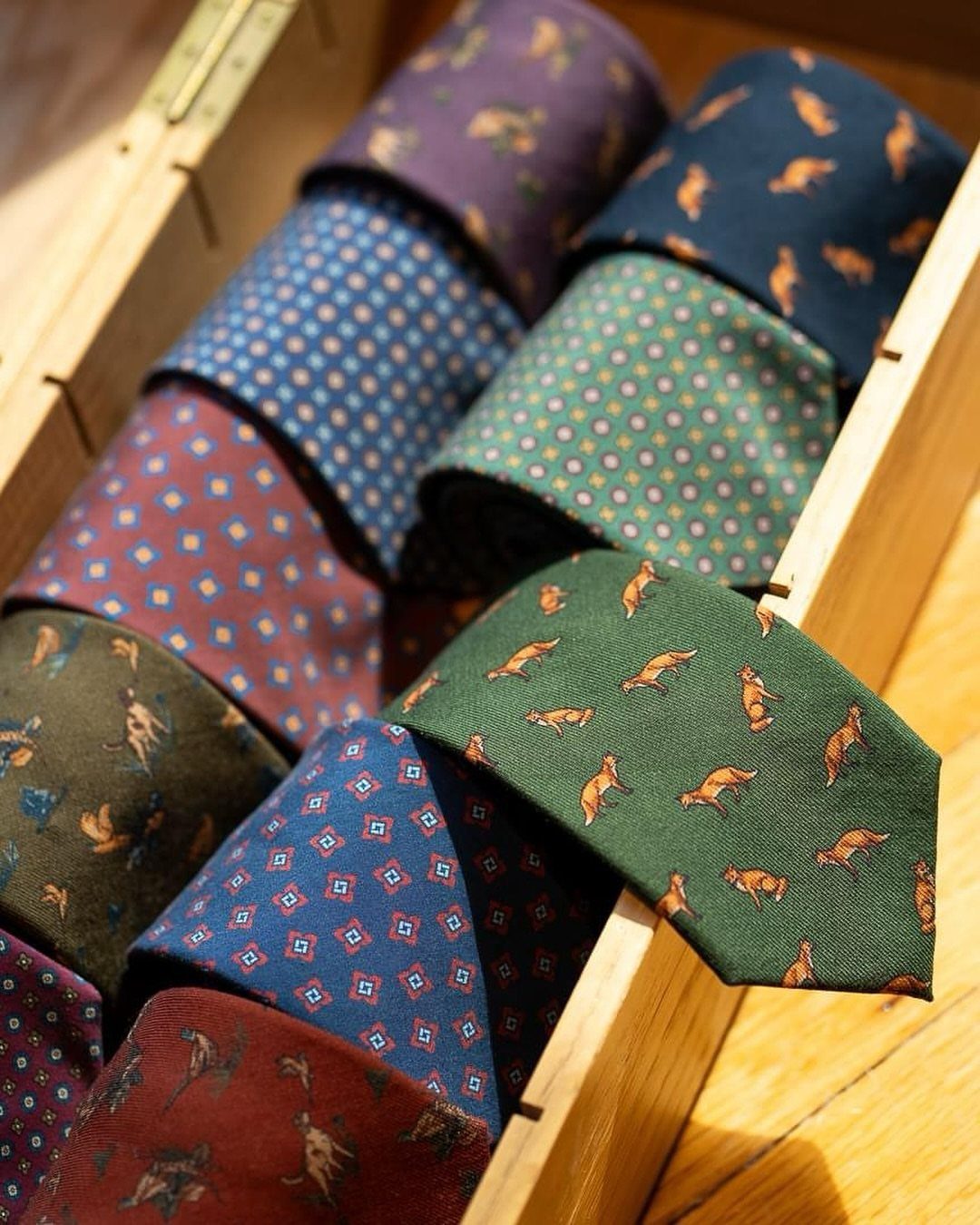 Various patterned neckties rolled inside a light wooden storage box.