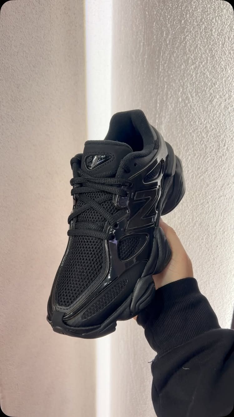A hand holding a black chunky mesh sneaker against a light wall.