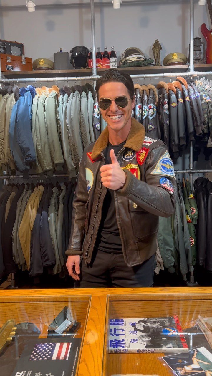 Smiling man in sunglasses wearing a brown leather flight jacket with colorful patches.