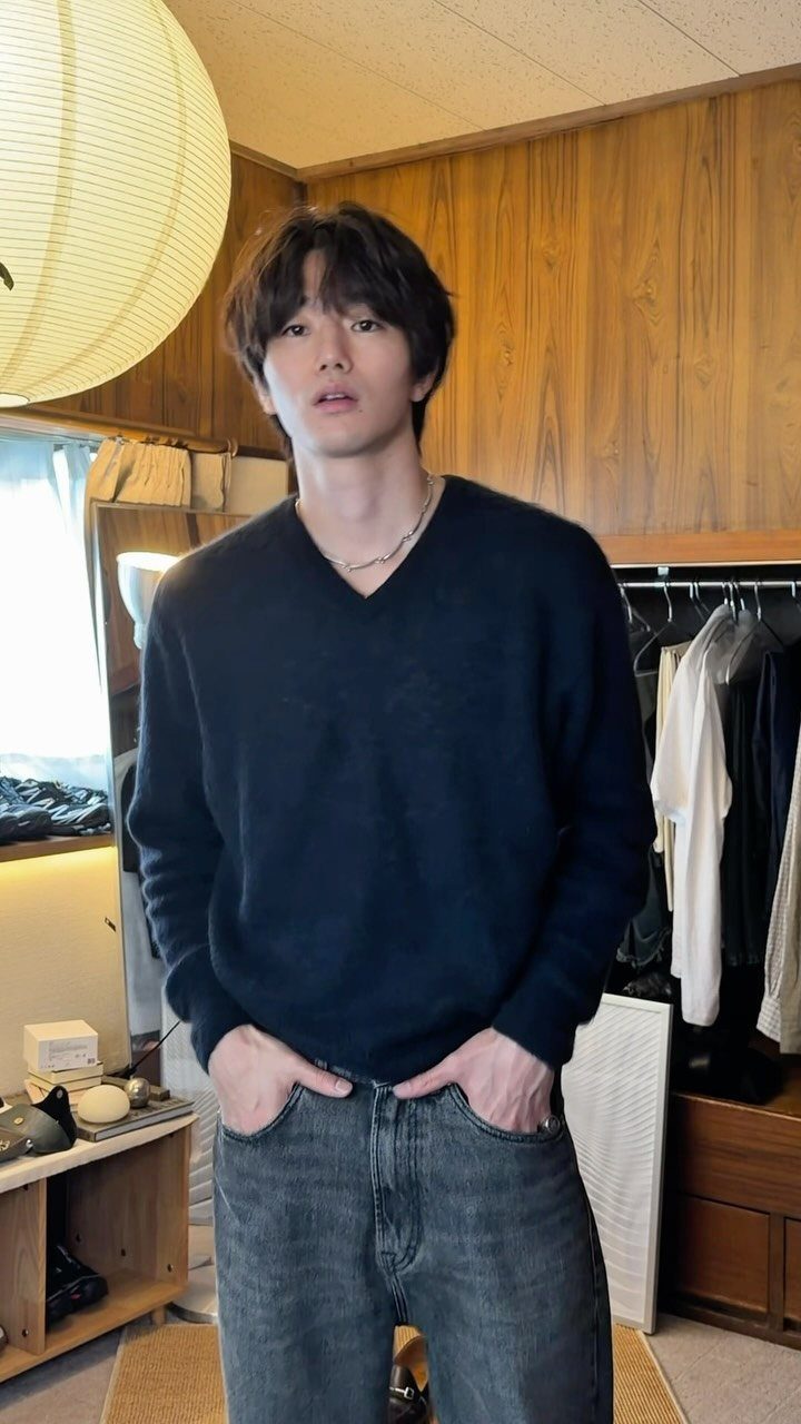 A young man wearing a dark navy V-neck sweater and blue denim jeans.