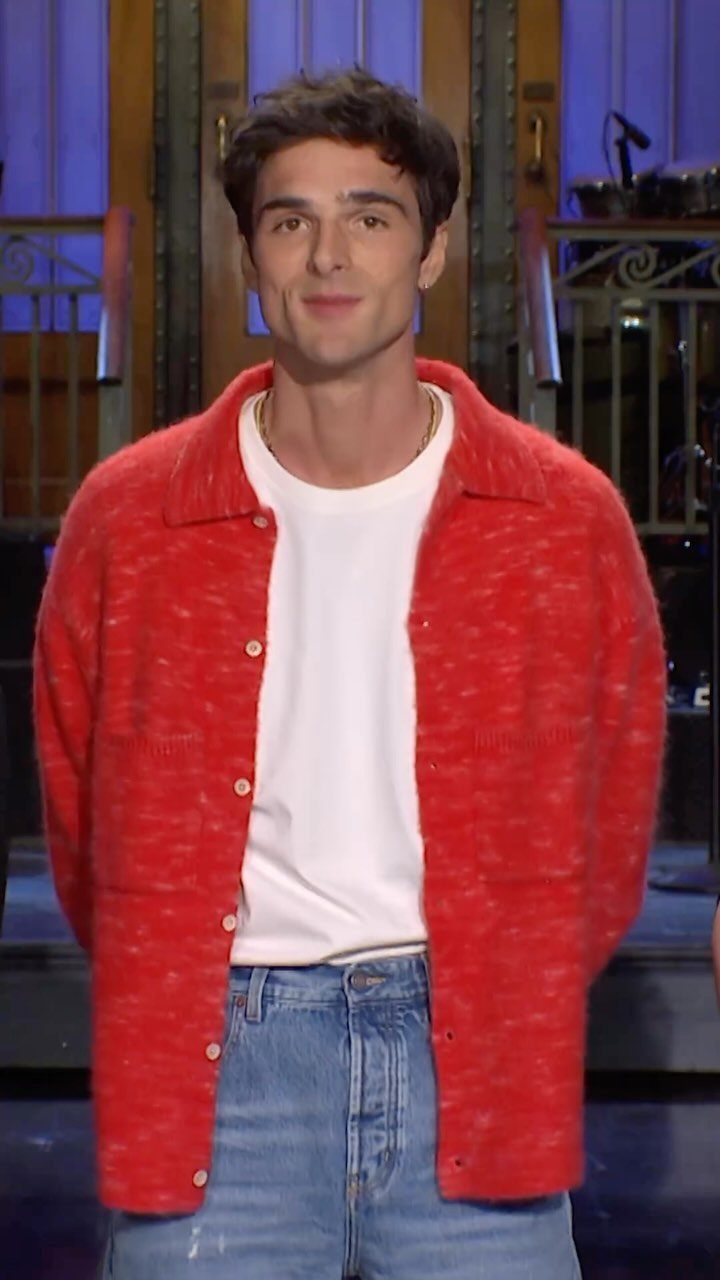A man wearing a bright red textured knit shirt over a white t-shirt and blue jeans.