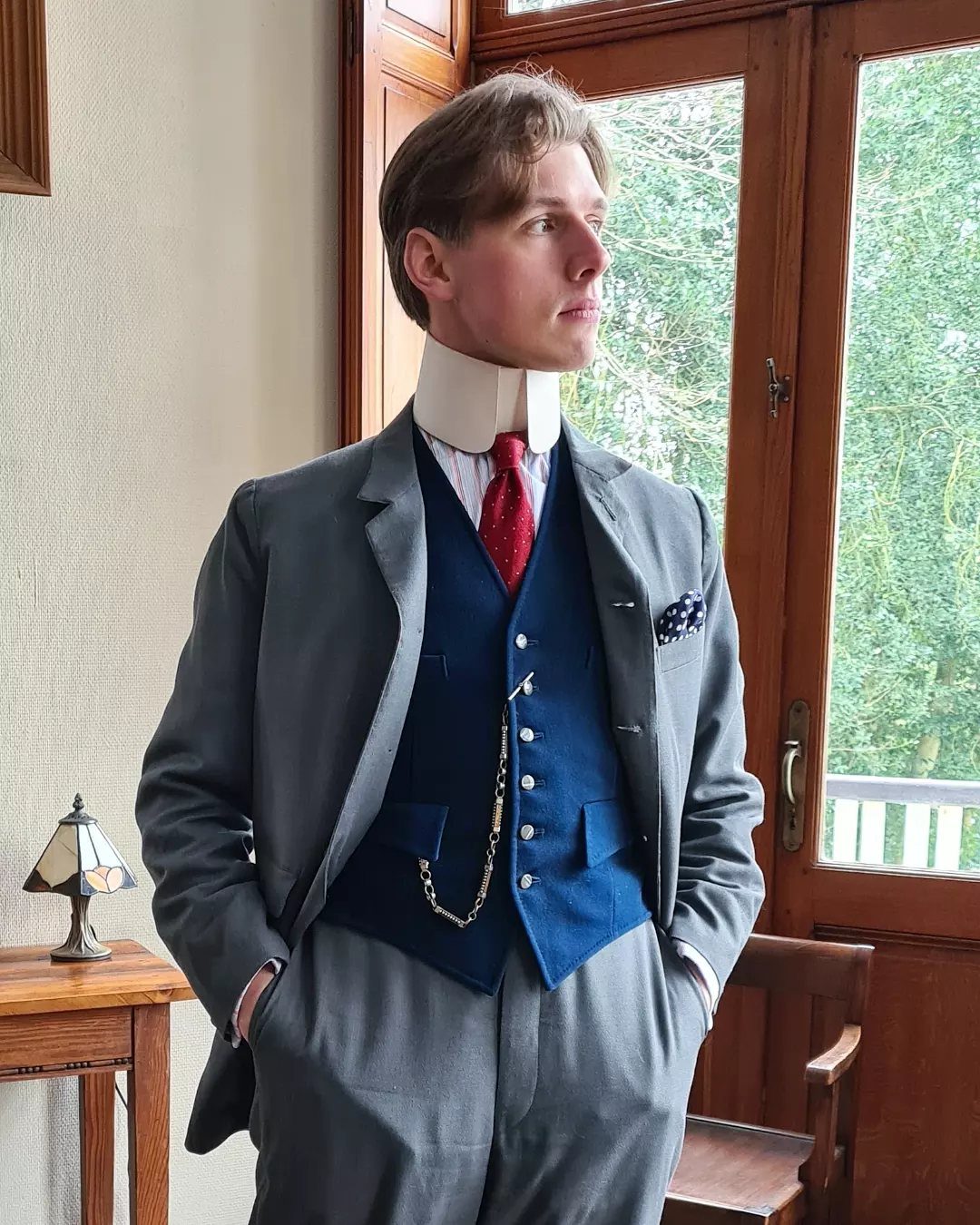 Man in a grey Victorian suit wearing a high white collar and a red necktie.