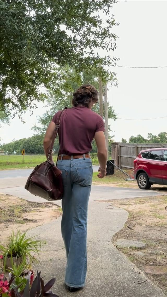 A man walking away wearing a maroon shirt and light blue denim bell bottom jeans.