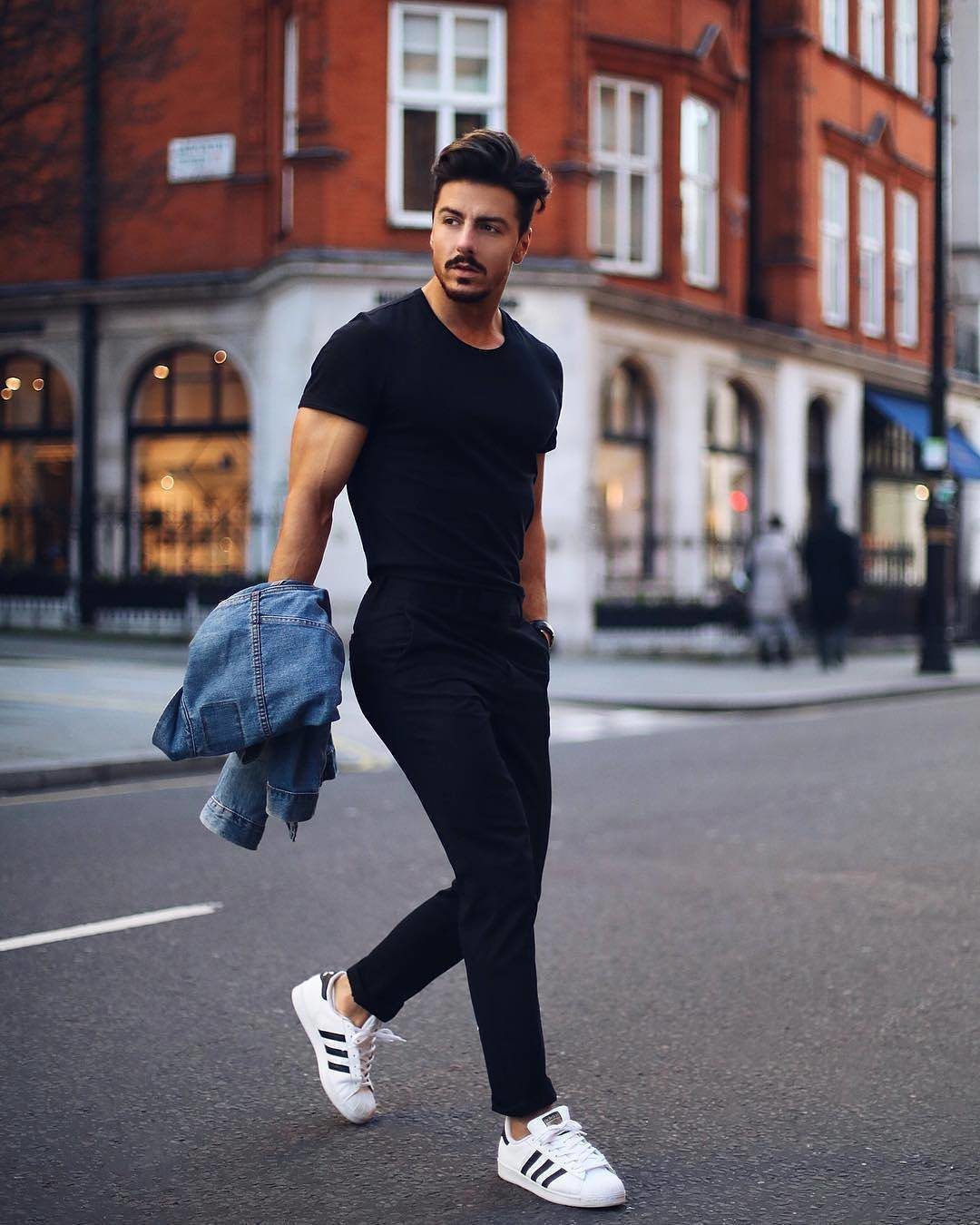 Man in an all black outfit and white sneakers walking on a city street.