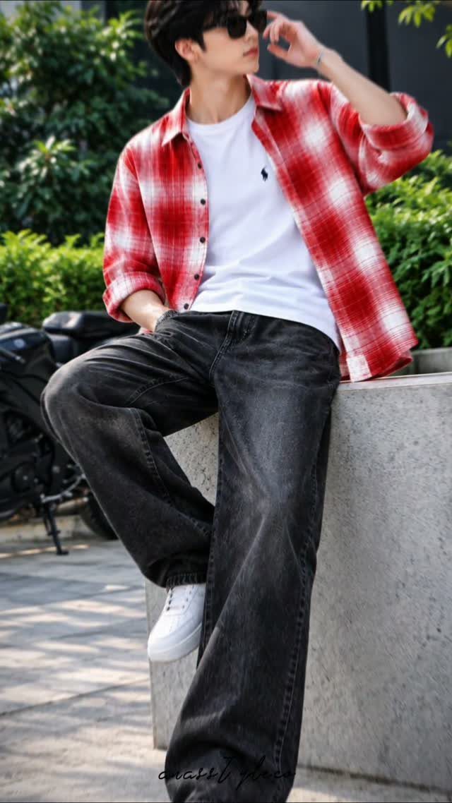 Man in a red flannel shirt, white t-shirt, black jeans, and white sneakers leaning against a wall.