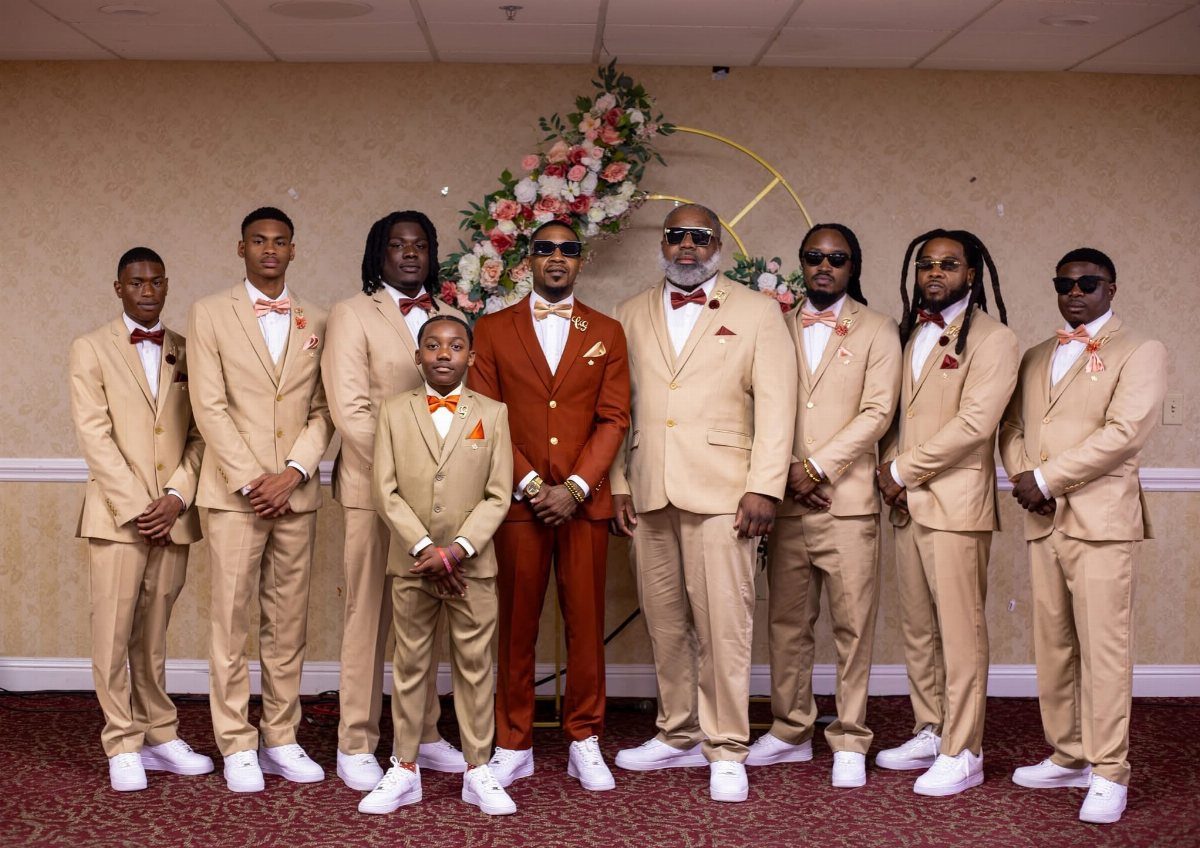 Men in tan suits and white sneakers posing together in a formal indoor setting.