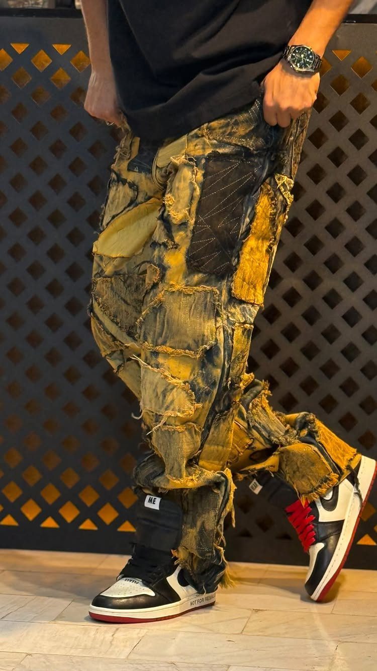 Person wearing heavily distressed and patched yellow denim jeans with black and white sneakers.
