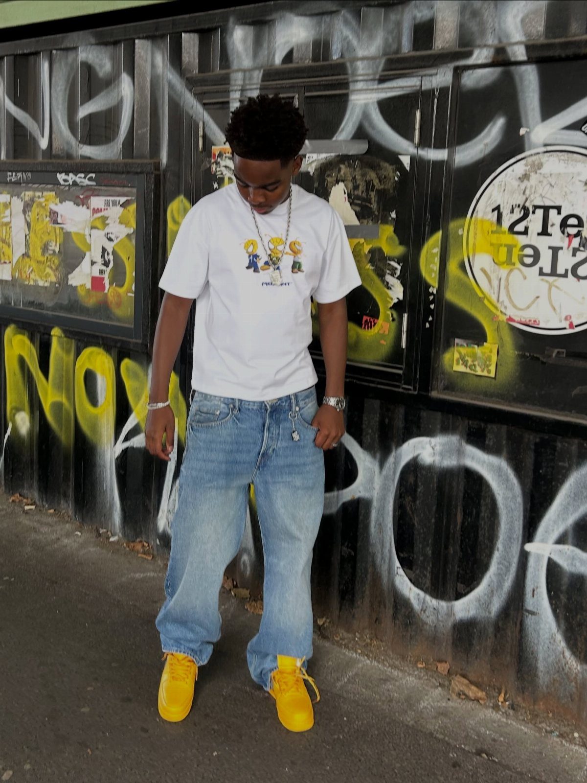 A person wearing light blue jeans and bright yellow sneakers standing against a graffiti wall.