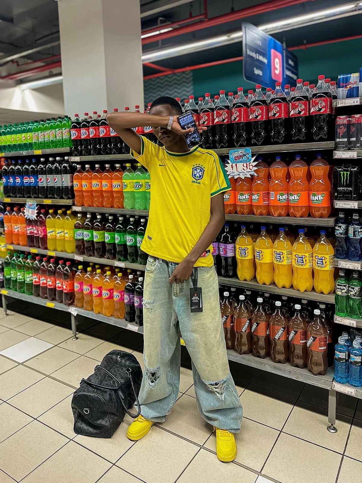 Person in a yellow jersey, baggy jeans, and yellow sneakers standing in a grocery aisle.