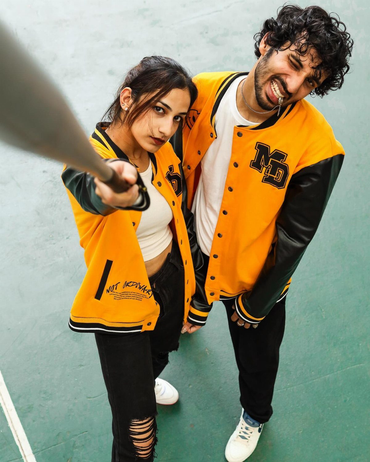 Two people wearing yellow and black varsity jackets posing together on a green floor.