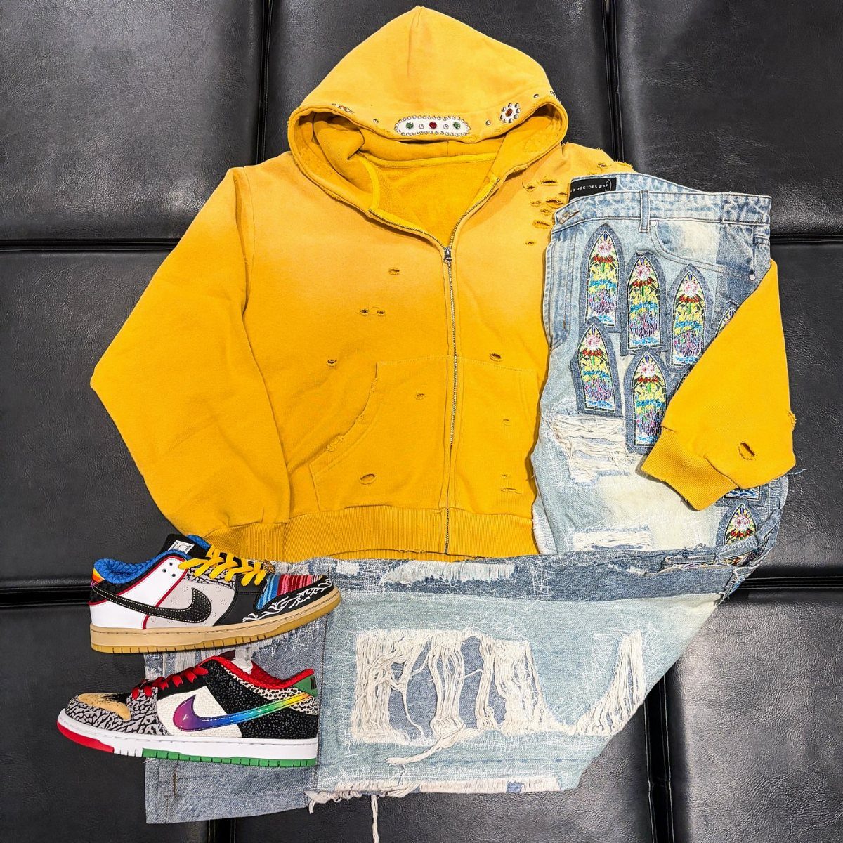 Yellow zip-up hoodie, distressed denim jeans, and colorful sneakers laid out on a black surface.