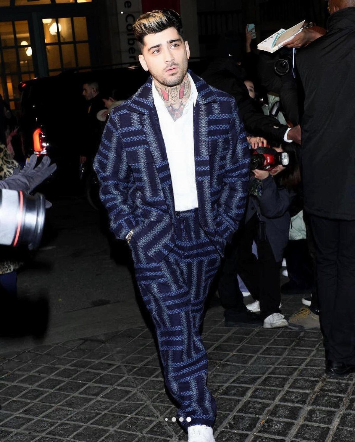 Zayn Malik walking through a crowd wearing a navy blue patterned suit and white shirt.