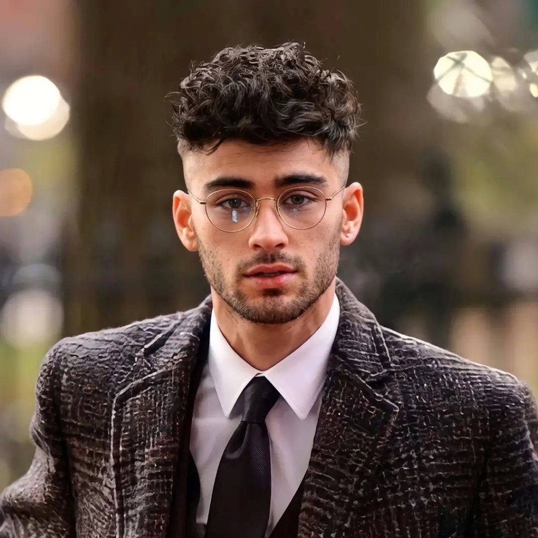 Zayn Malik wearing glasses, a white shirt, black tie, and a textured grey blazer.