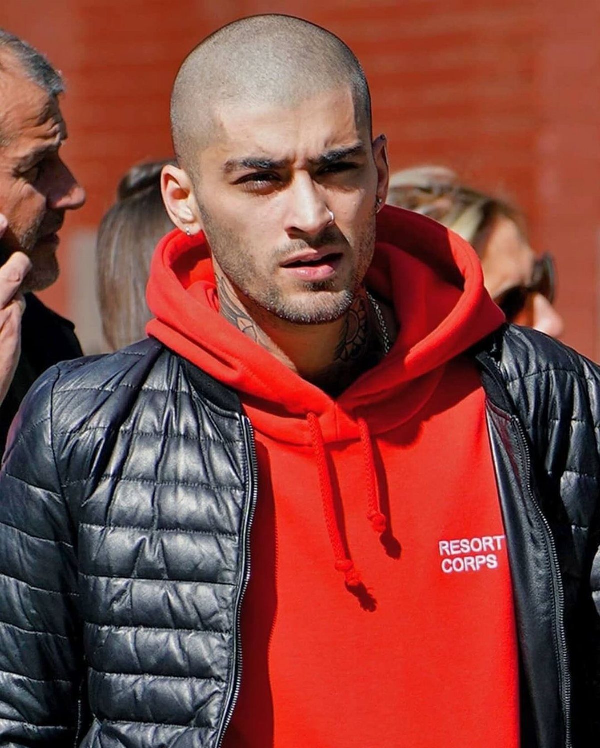 A man wearing a red Resort Corps hoodie under a black quilted jacket.