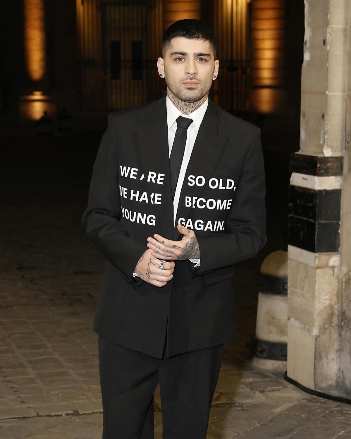Man in a black suit with white text on the jacket and a black tie.